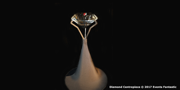 A large, clear diamond centerpiece is displayed on a tall, conical stand with a black background.