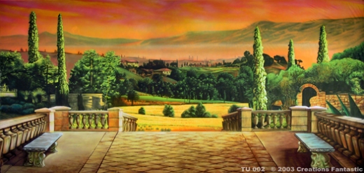 A scenic view depicts a vibrant Tuscan countryside landscape with trees, fields, and rolling hills at sunset, viewed from a stone terrace with two benches.