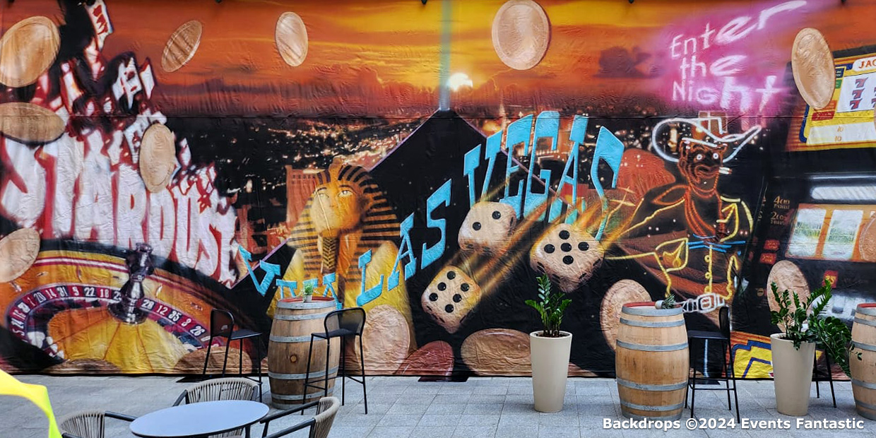 A vibrant mural featuring casino-themed imagery, including dice, poker chips, and a cowgirl. Set against a cityscape backdrop with tables and chairs in the foreground, the piece captures the lively spirit of Las Vegas. Viva Las Vegas vibes pulse through every brushstroke!