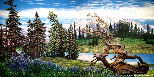 A scenic landscape featuring a twisted tree in the foreground, a small lake, tall evergreen trees, and snow-capped mountains in the background under a blue sky—the perfect snapshot of the great outdoors.