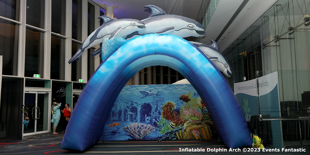 Inflatable Dolphin Arch at an indoor event, featuring dolphins on top and an underwater scene backdrop. 2023.