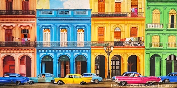 Colorful street scene featuring vibrant, multi-colored buildings and vintage cars parked along the road. The buildings are painted in shades of blue, yellow, orange, and green.