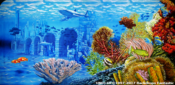An underwater scene featuring ruins of a stone structure, colorful coral reefs, various fish, and a swimming shark under clear blue water.