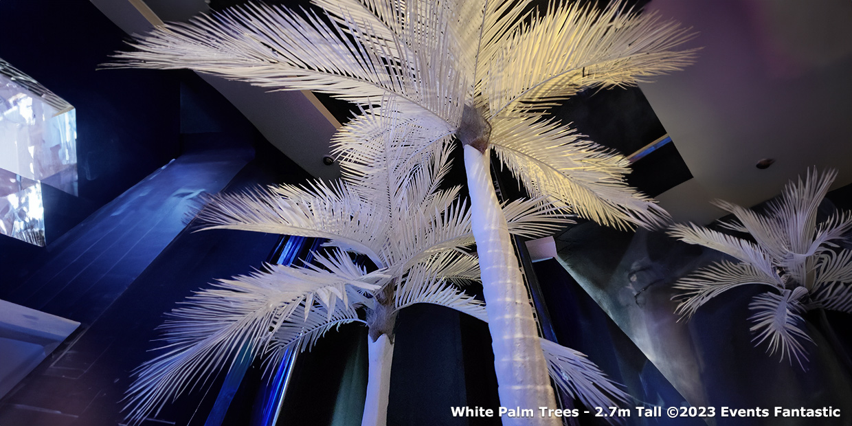 Tall white palm tree props reaching up to 2.7m inside a modern indoor space.