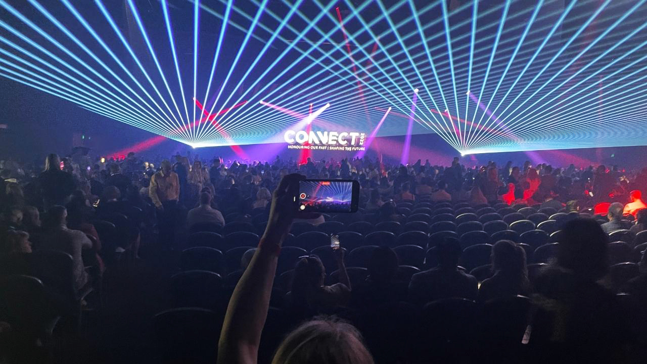 Large conference event with guests dancing and recording the stage show with their mobile phones.