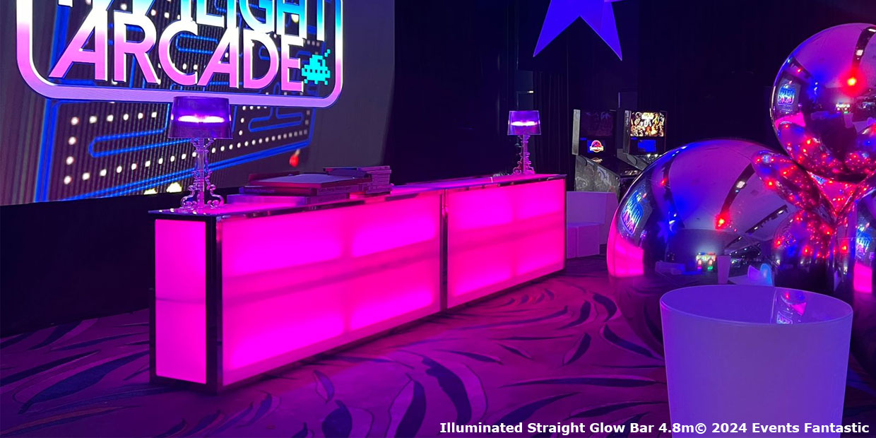 Illuminated 4.8m wide Glow Bar with purple lighting, surrounded by metallic decor and arcade signage, set up in an indoor event space.