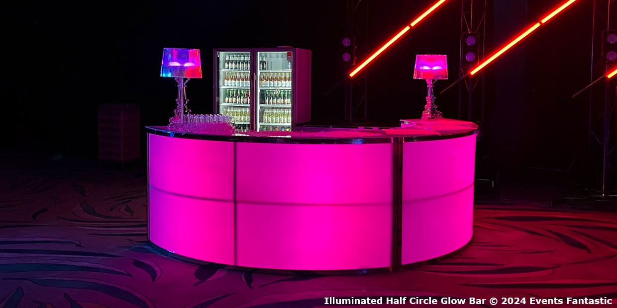An illuminated glow bar, forming a half-circle and glowing pink, features two lamps and a stocked mini-fridge, set against dark surroundings.