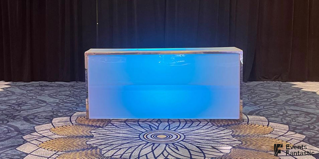 An illuminated straight glow bar shines in blue on a patterned carpet, set against a dark curtain background.