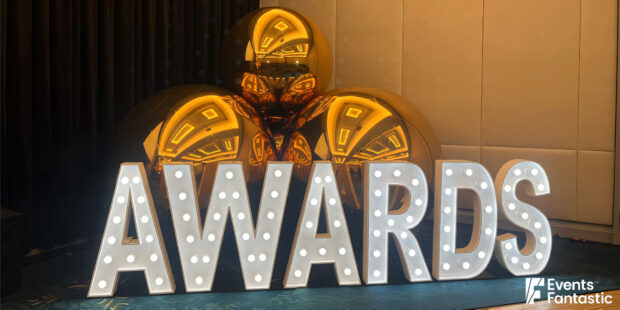 Large lit letters spelling "AWARDS" stand prominently in front of three inflatable gold mirror balls.
