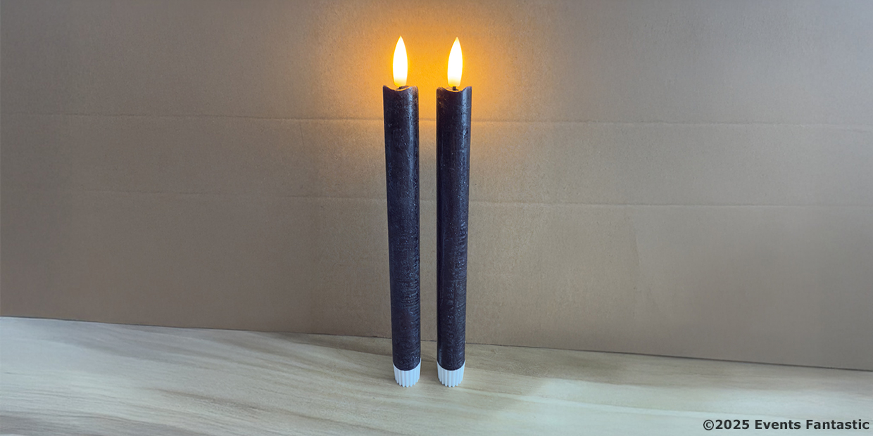 Two Black Tapered LED Candles with yellow flame-shaped lights stand upright on a wooden surface against a plain cardboard background.