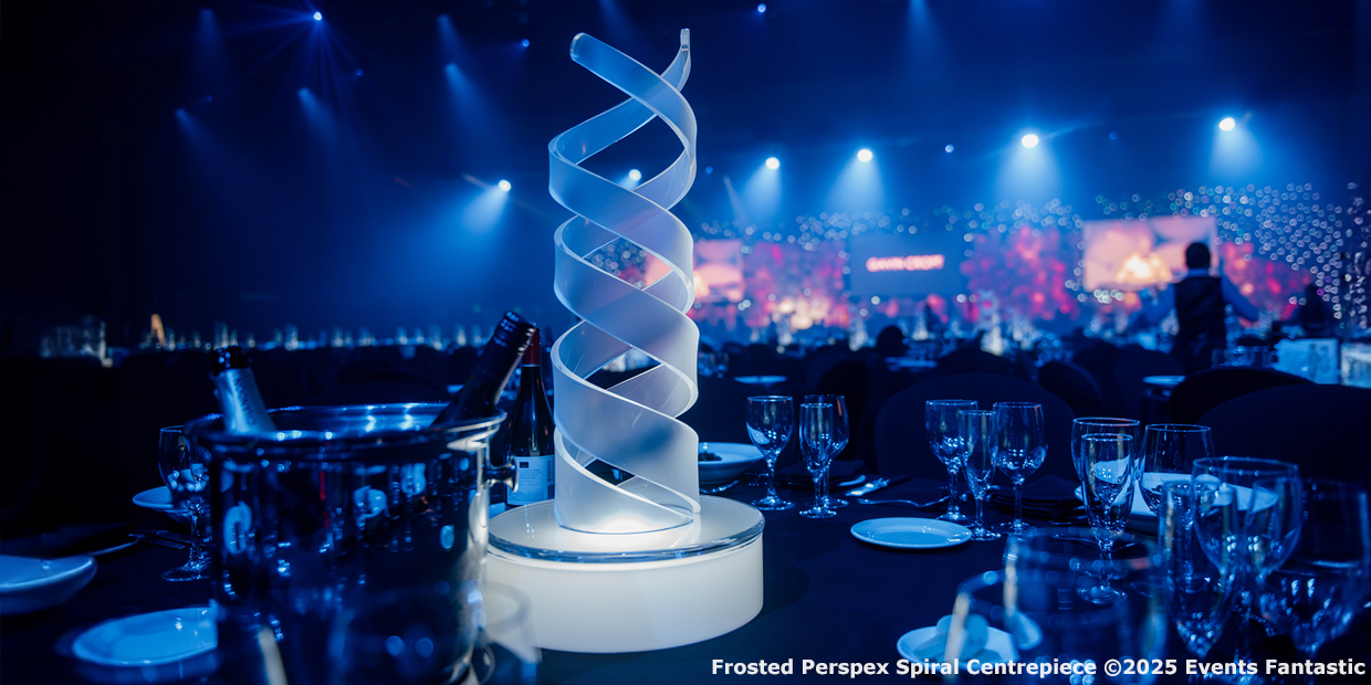 A frosted Perspex spiral centrepiece sits on a round table set with glassware and an ice bucket at a dimly lit event venue with blue ambient lighting.