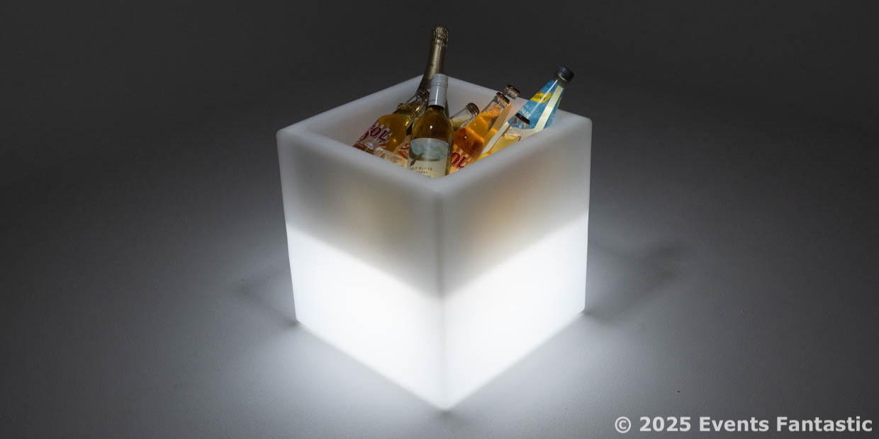 A glowing white square ice bucket holds several bottles of beverages, its illuminated design standing out against a plain background.