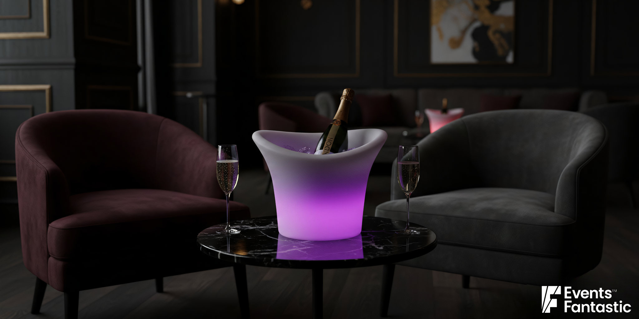 A champagne bottle in a glow ice bucket with two filled glasses sits on a round table between two armchairs in a dimly lit lounge.