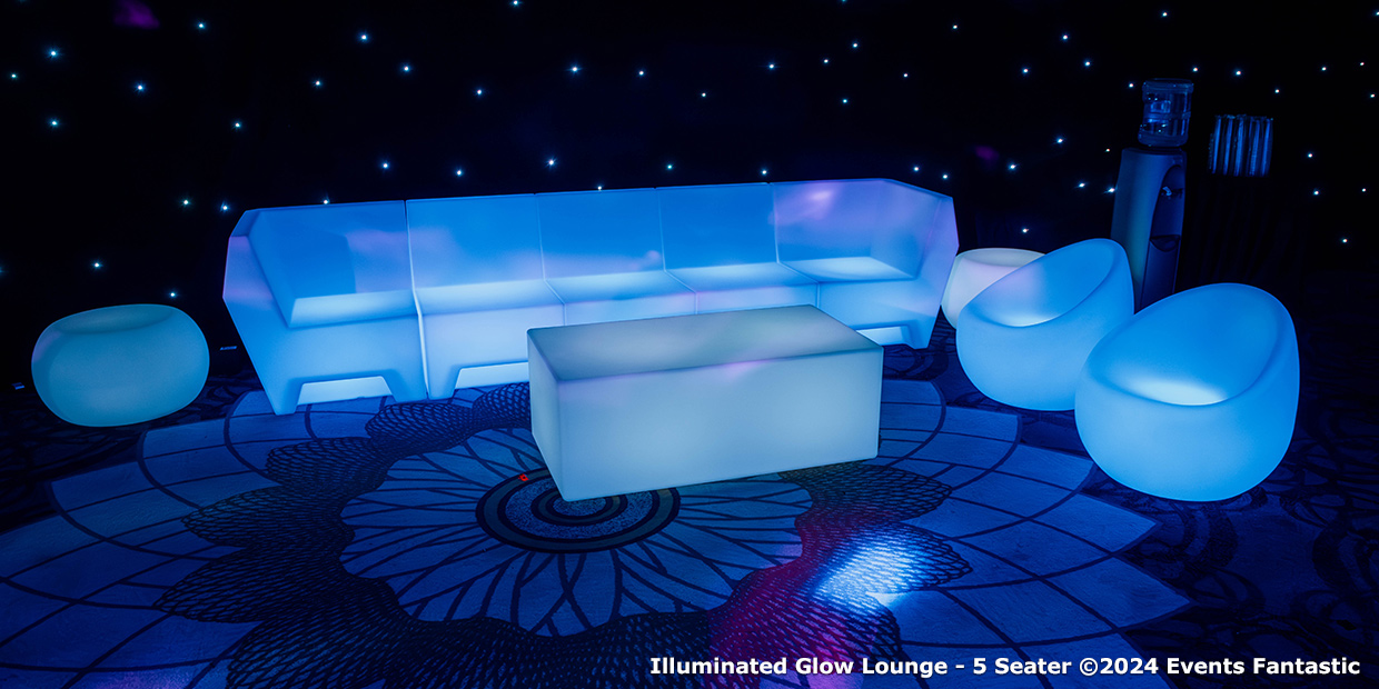 A white illuminated glow lounge set featuring a five-seater sofa, two chairs, two round stools, and an Illuminated Glow Bar table sits on a patterned floor with a starry backdrop.