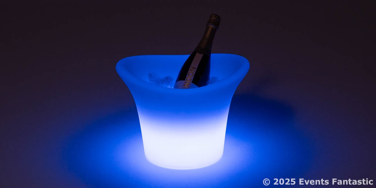 A glowing, blue-lit illuminated ice bucket with a bottle of sparkling wine inside sits elegantly on a dark surface.