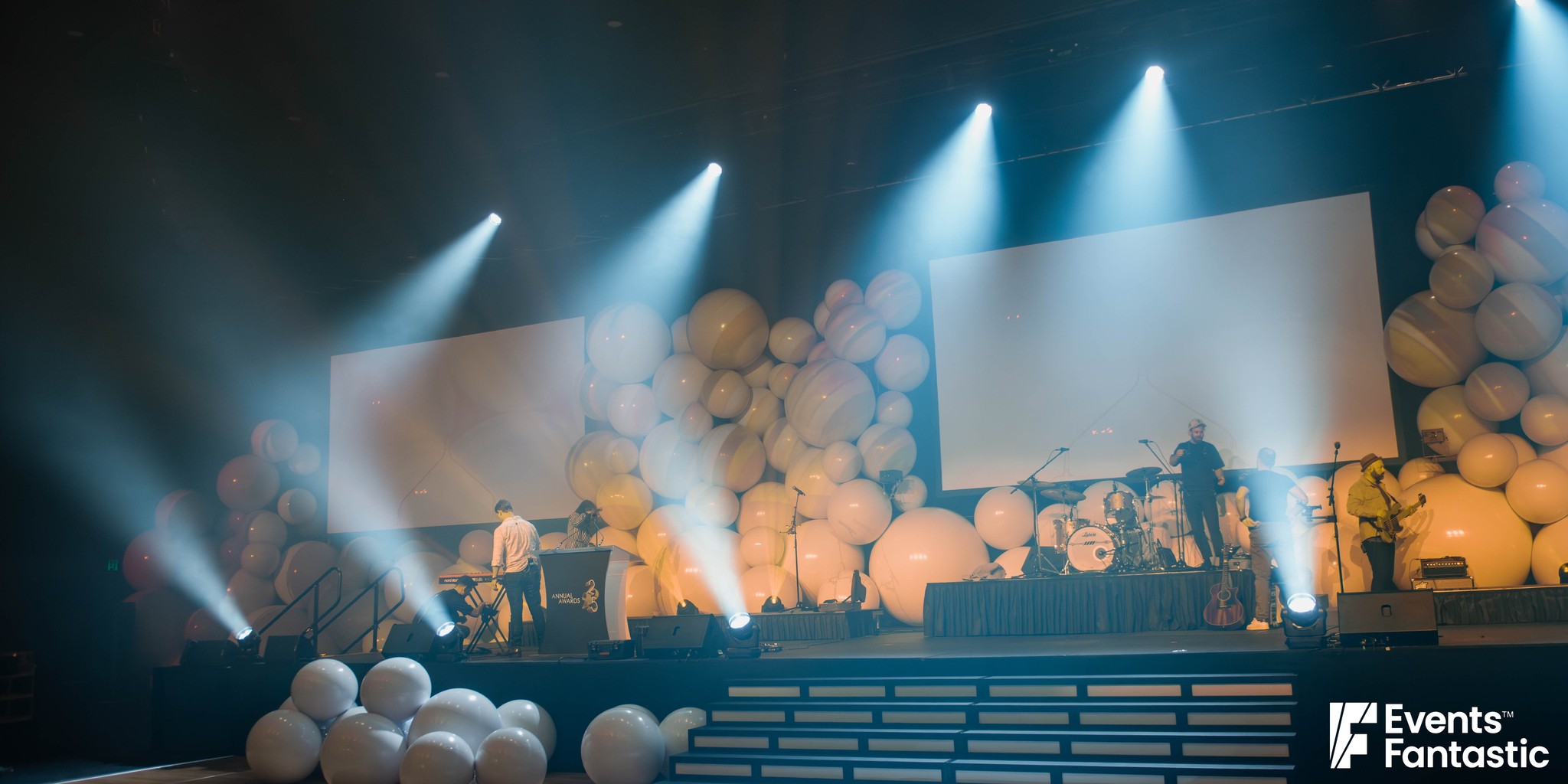 Stage set with walls of inflatable white matt balls in warm light and a pile of balls on the floor, hire from Events Fantastic.