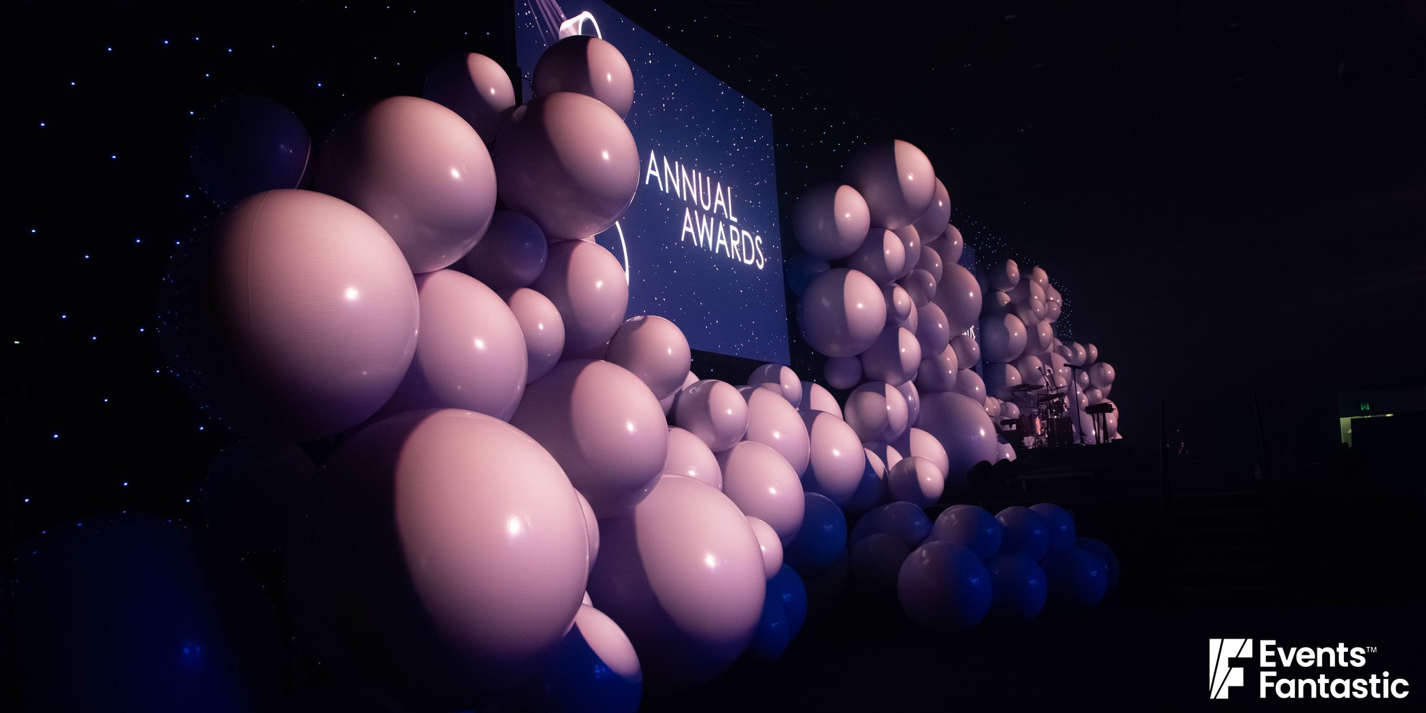 Close view of a stage wall of inflatable white matt balls in mixed sizes, lit lilac, hire from Events Fantastic.