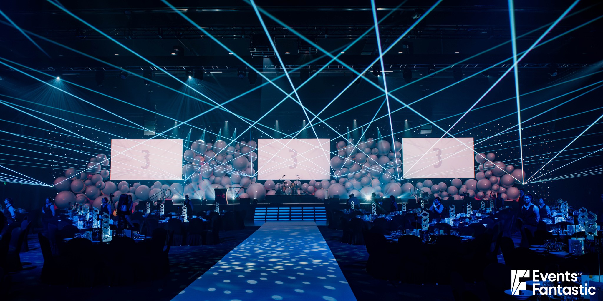 Ballroom set for an awards night with a wall of inflatable white matt balls behind three screens under blue laser light, hire from Events Fantastic.