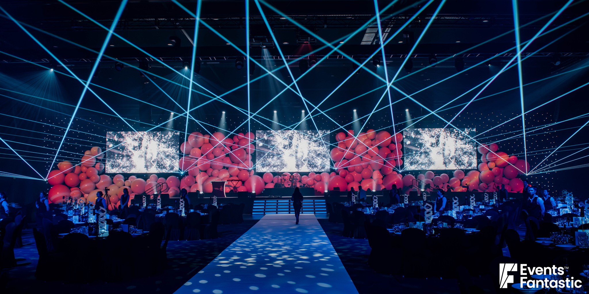 Wall of inflatable white matt balls washed red behind the stage screens at an awards night, hire from Events Fantastic.